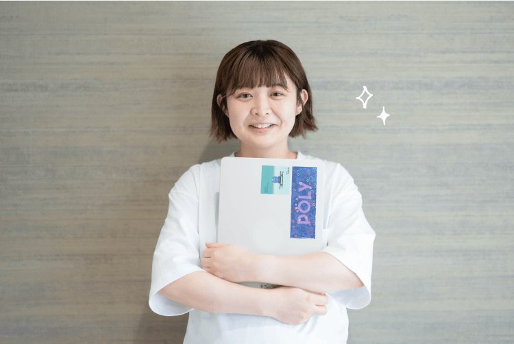 グレーの壁を背景に、書類ファイルを抱えて微笑むあかりさん