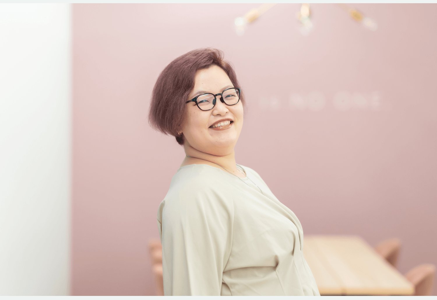 桜色の壁を背景に振り返って微笑むayaさん