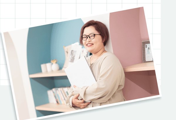 本棚を背景に書類を抱えて微笑むayaさん