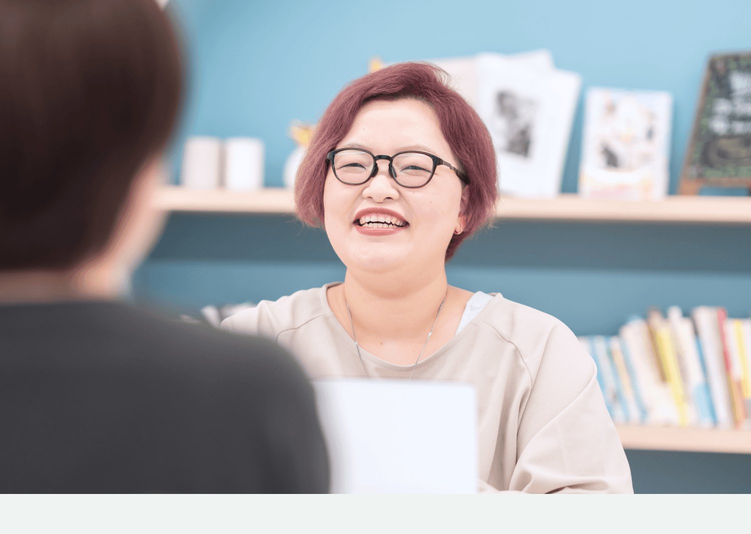 書棚を背景に対面で話すayaさん