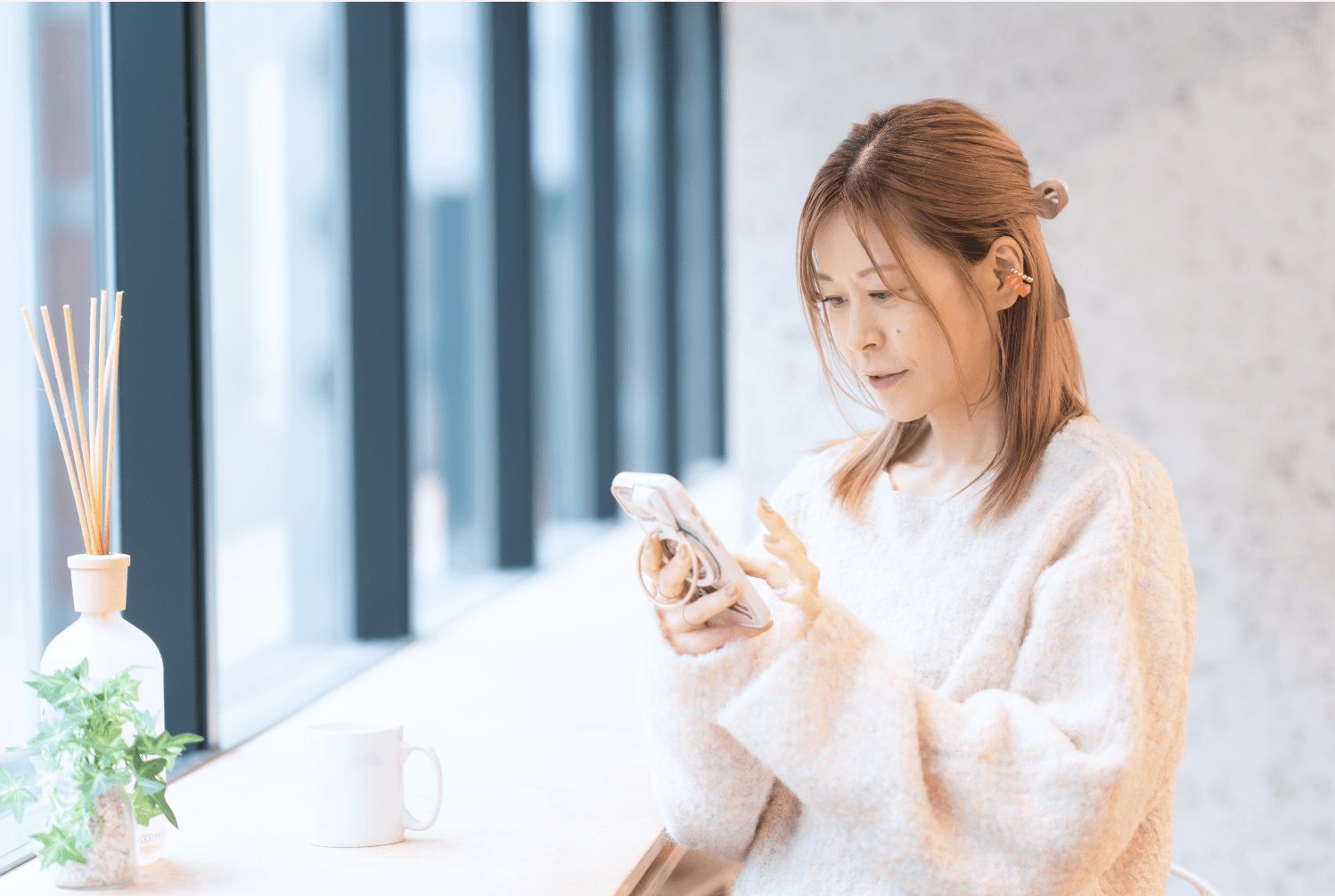 窓辺のテーブルでスマートフォンを操作しながら微笑むゆるみさん