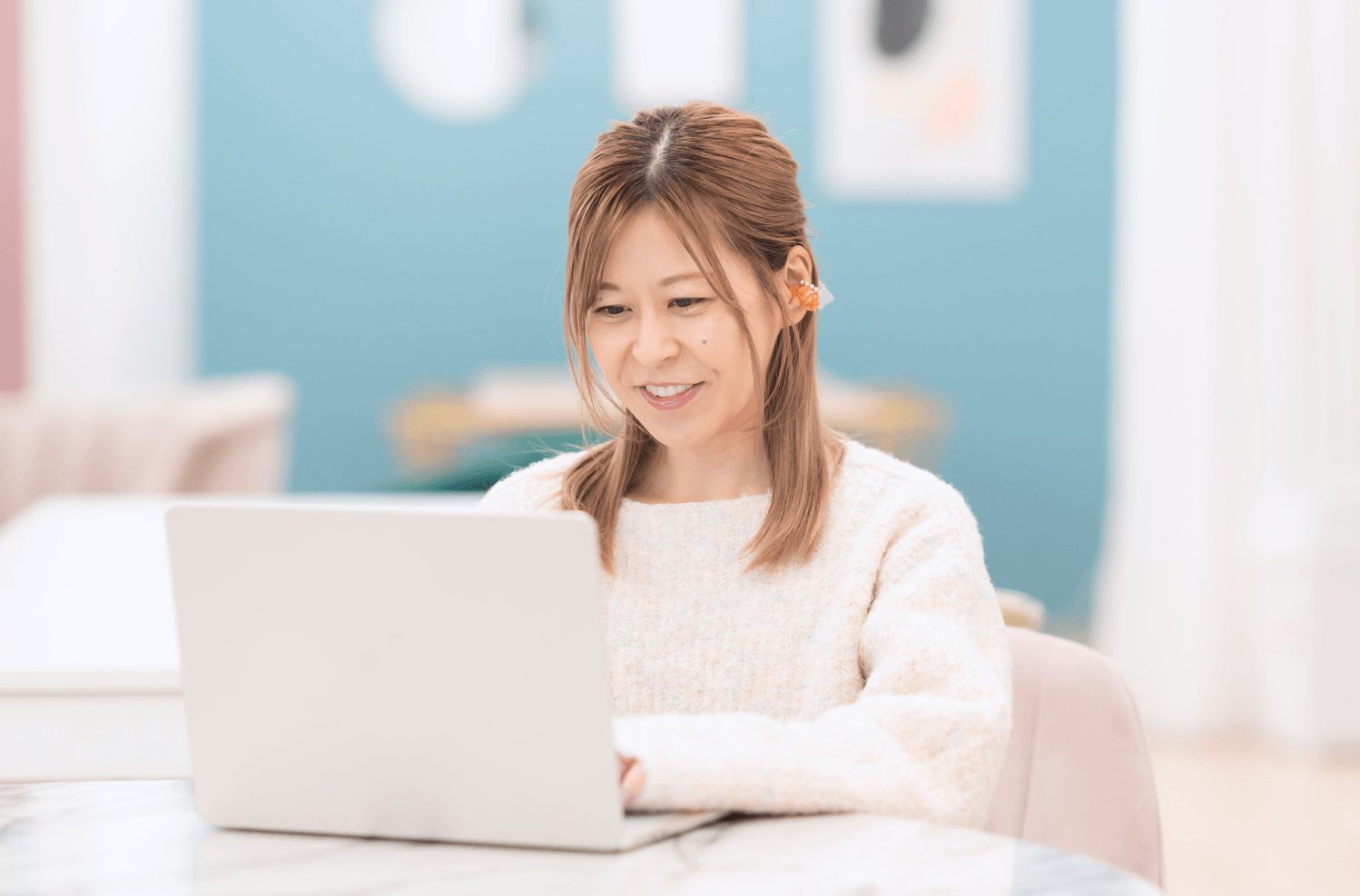 青い壁のインテリアの部屋でノートPCに向かい微笑むゆるみさん