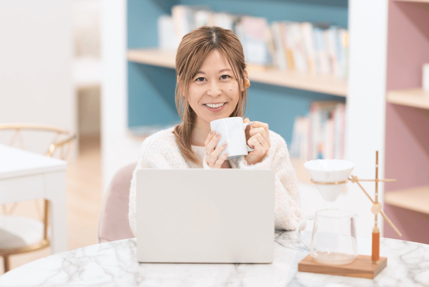 本棚を背景に、マグカップを手にノートPCの前で微笑むゆるみさん