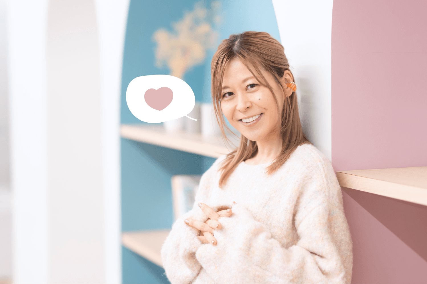 本棚とピンクの壁を背景に、ハート型の吹き出し装飾つきで微笑むゆるみさん