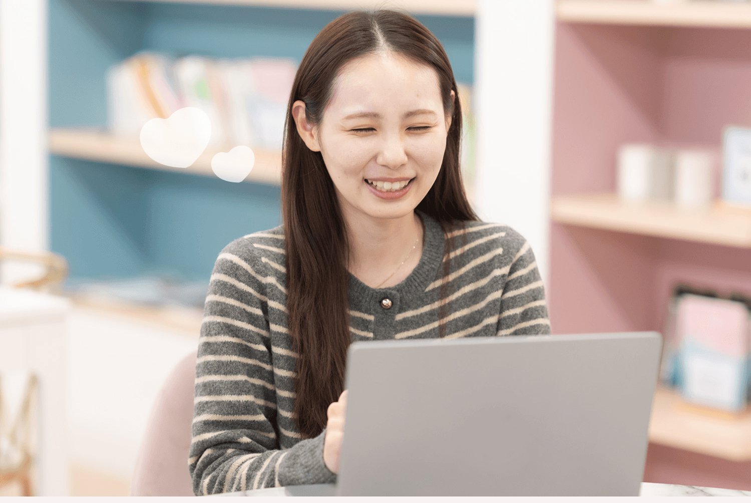 木目テーブルでノートPCを操作しながら微笑む莉央奈さん