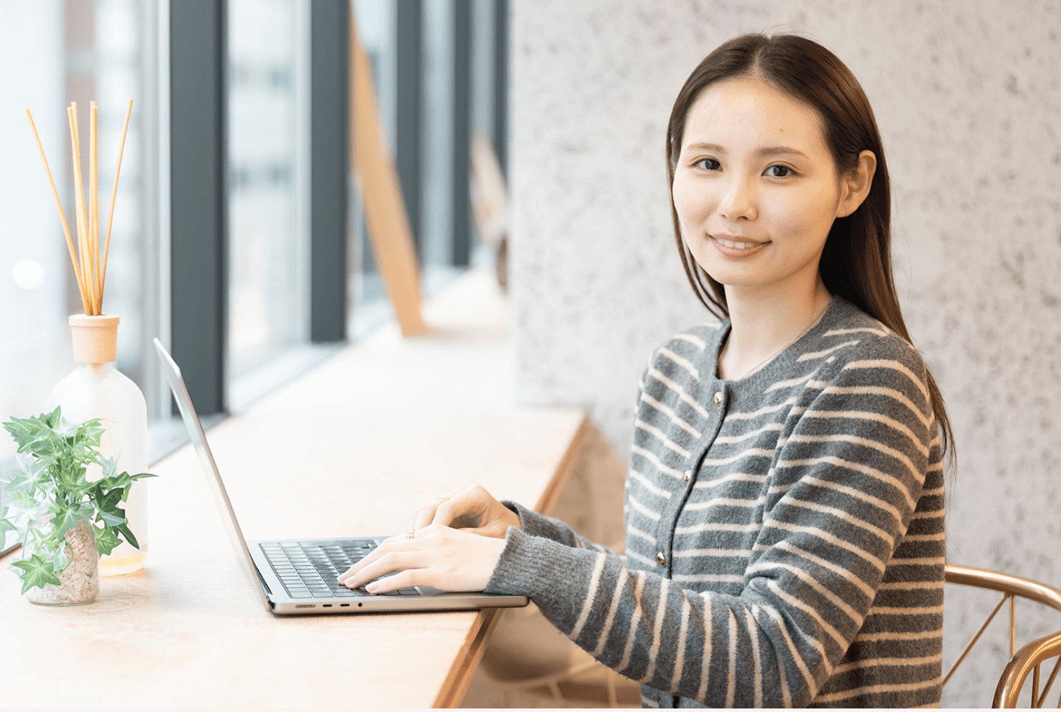 カフェの窓際の席でノートPCを操作しながら微笑む莉央奈さん