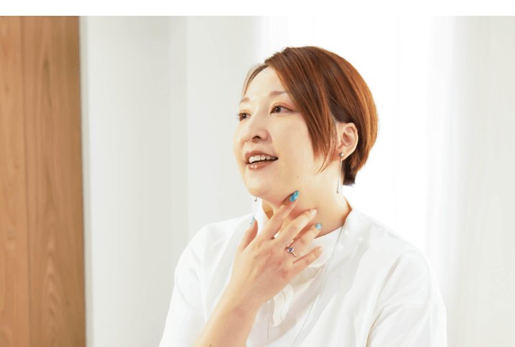 白いトップスの女性が窓辺で笑顔で話しているインタビューカット
